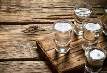 Glasses with vodka on an old board on wooden background.