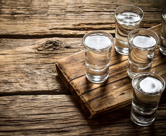 Glasses with vodka on an old board on wooden background.