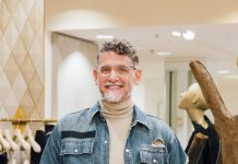 Meet David Crain: One of Metro Detroit’s Most Beloved Personal Shoppers Posing in Somerset’s Saks Fifth Avenue, David Crain rocks double denim (jacket and jeans by Helmut Lang) with an Isaia turtleneck, a Rolex watch, and Prada boots.
