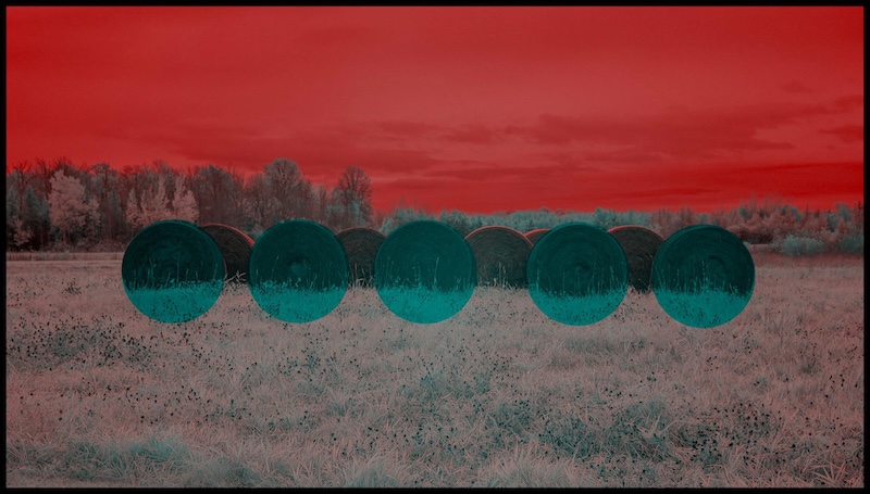 Bluish hay bales in a field with a backdrop of trees and a red sky, on display at the DIA's Contemporary Anishinaabe Art: A Continuation
