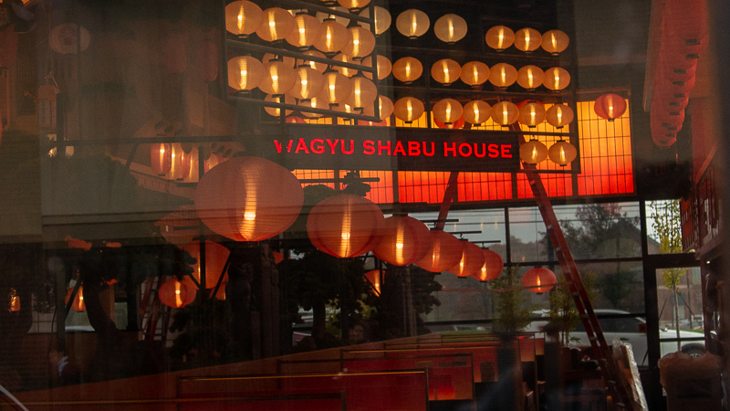 A glimpse of the inside of Wagyu Shabu House, feauring pendant lighting, booths, and a red sign with the restaurant's name at Sakura Novi after the dedication of Sakura Gardens