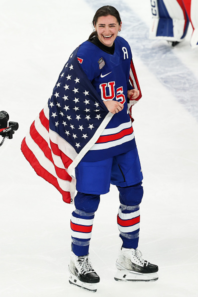Megan Keller #5 of Team United States celebrates winning the gold medals with the national flag after the team's 2-1 overtime victory in the Women's Gold Medal match between the United States and Canada on day 13 of the Milano Cortina 2026 Winter Olympic games at Milano Santagiulia Ice Hockey Arena on February 19, 2026 in Milan, Italy. 