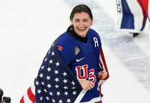 Megan Keller #5 of Team United States celebrates winning the gold medals with the national flag after the team's 2-1 overtime victory in the Women's Gold Medal match between the United States and Canada on day 13 of the Milano Cortina 2026 Winter Olympic games at Milano Santagiulia Ice Hockey Arena on February 19, 2026 in Milan, Italy.