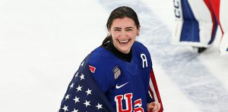 Megan Keller #5 of Team United States celebrates winning the gold medals with the national flag after the team's 2-1 overtime victory in the Women's Gold Medal match between the United States and Canada on day 13 of the Milano Cortina 2026 Winter Olympic games at Milano Santagiulia Ice Hockey Arena on February 19, 2026 in Milan, Italy.