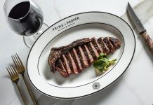 Plated cut steak with utensils and a glass of red wine.