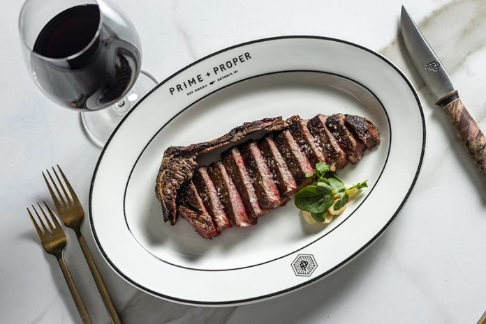 Plated cut steak with utensils and a glass of red wine.