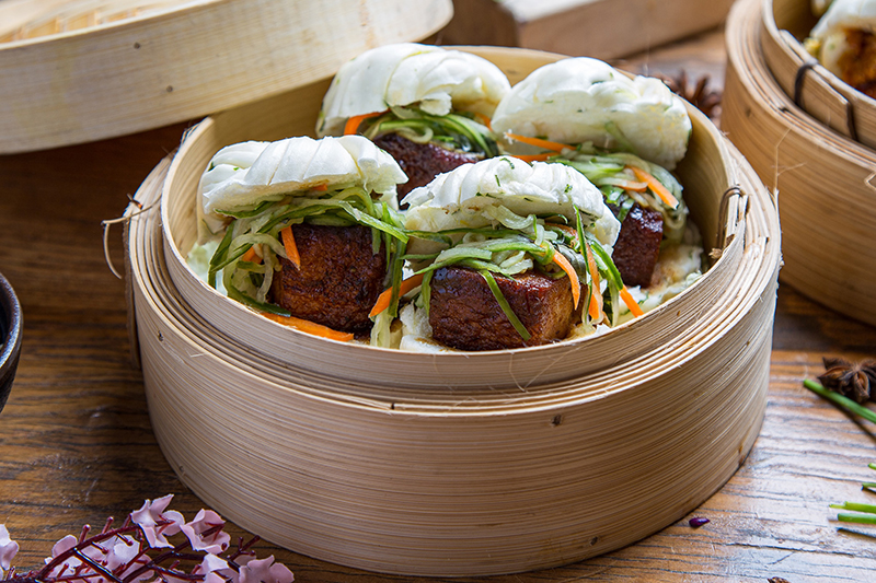 The pork belly bao buns are steamed, and served with pickled veggies on top.