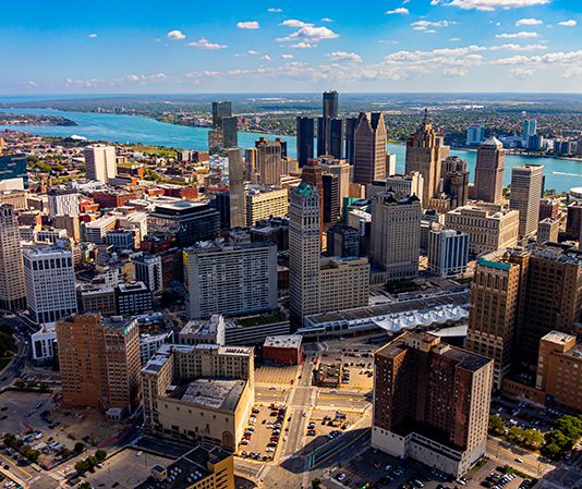 Drone aerial photo of downtown Detroit, Michigan with skyscrapers and the Detroit River on a sunny day.